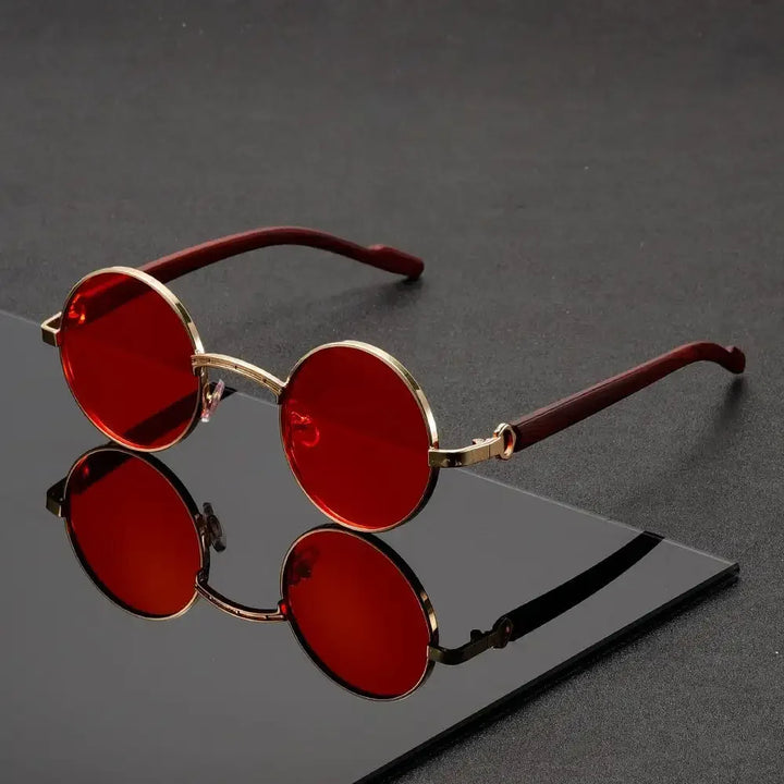 Red sunglasses with gold frames on a reflective black surface
