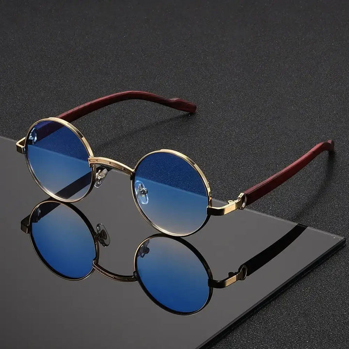 Round sunglasses with blue lenses and gold frames on a reflective surface.