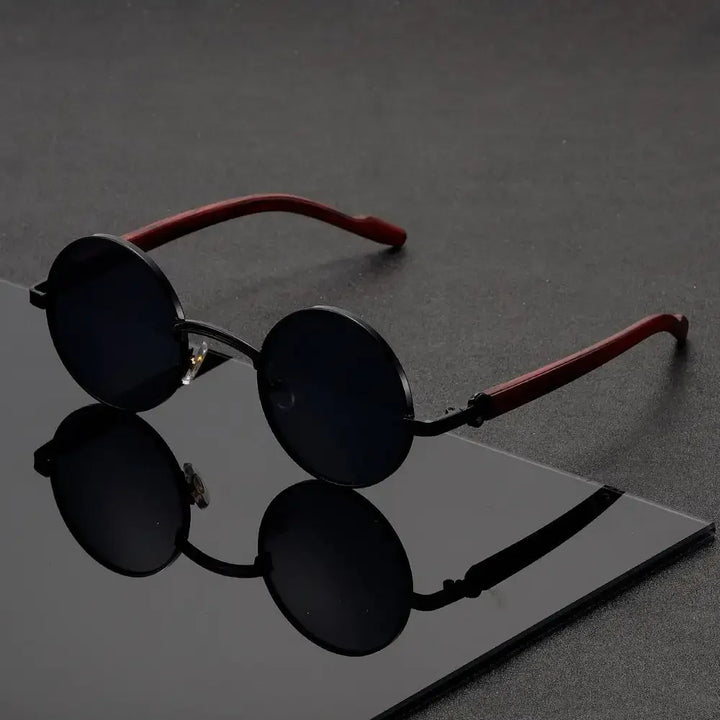 Black round sunglasses with red frames on a reflective surface