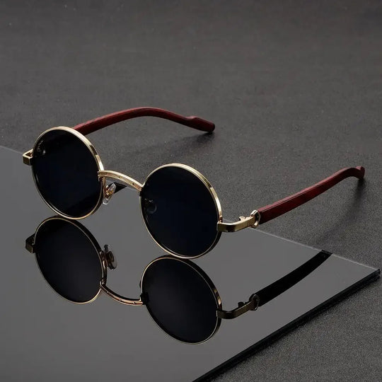 Round sunglasses with gold frames and dark lenses on a reflective surface.